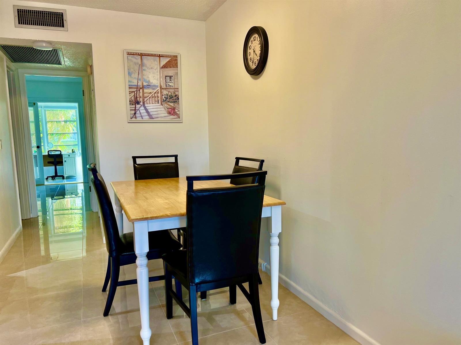 A dining area features a light wood table with four black chairs and a wall clock — 1011 Harwood C # 1011, Deerfield Beach FL 33442, DEERFIELD BEACH, FL