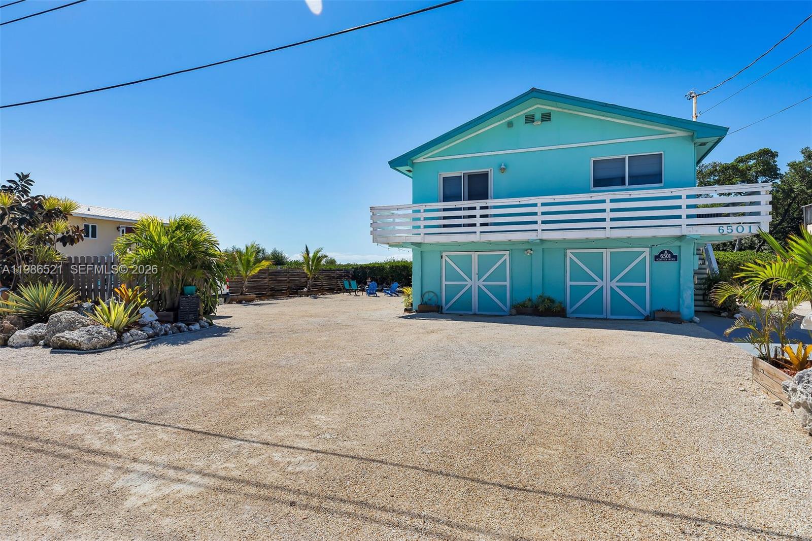 A two-story turquoise house with a white balcony stands above a gravel driveway — 6501 Oceanview Ave, Marathon FL 33050, MARATHON, FL