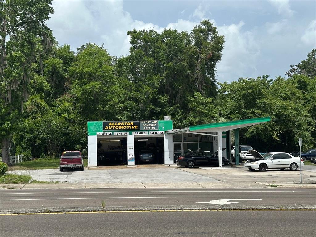 An exterior view of an automotive repair shop with a green sign and several parked cars — 706/720 NW 13TH STREET, GAINESVILLE, FL