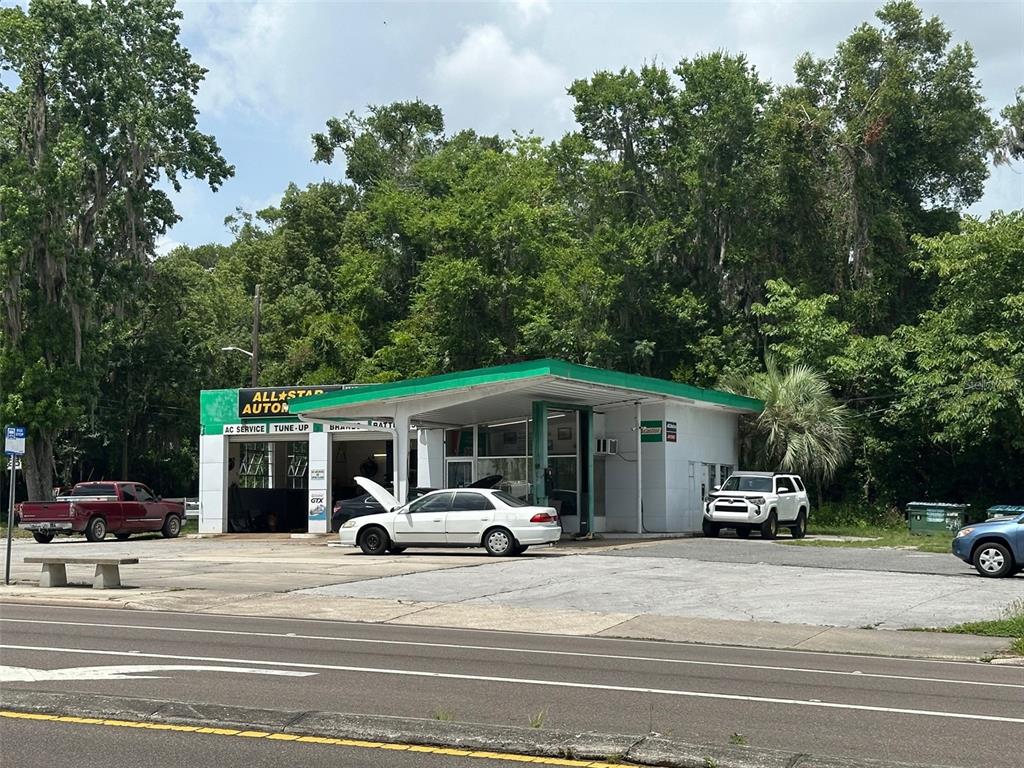 A white automotive repair shop with a green roof sits beside a road with trees — 706/720 NW 13TH STREET, GAINESVILLE, FL