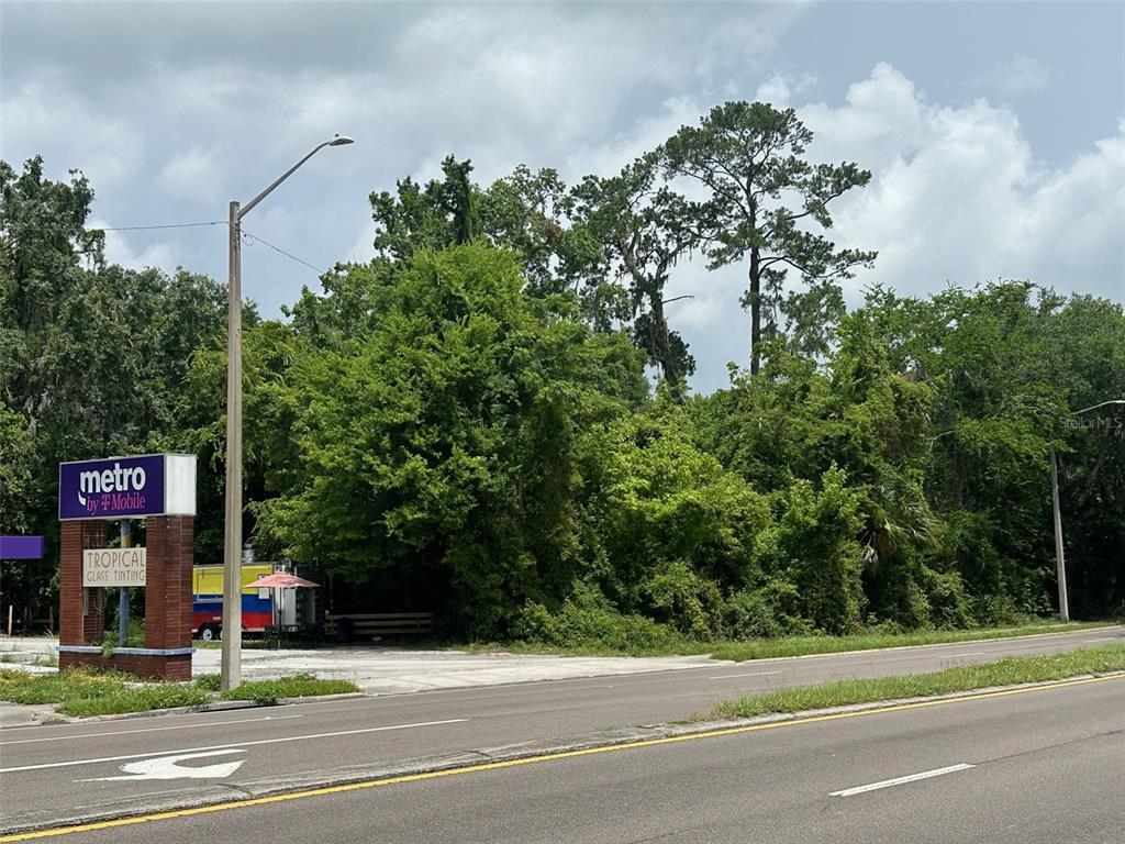 A vacant, wooded lot sits next to a commercial sign and a small food trailer — 706/720 NW 13TH STREET, GAINESVILLE, FL