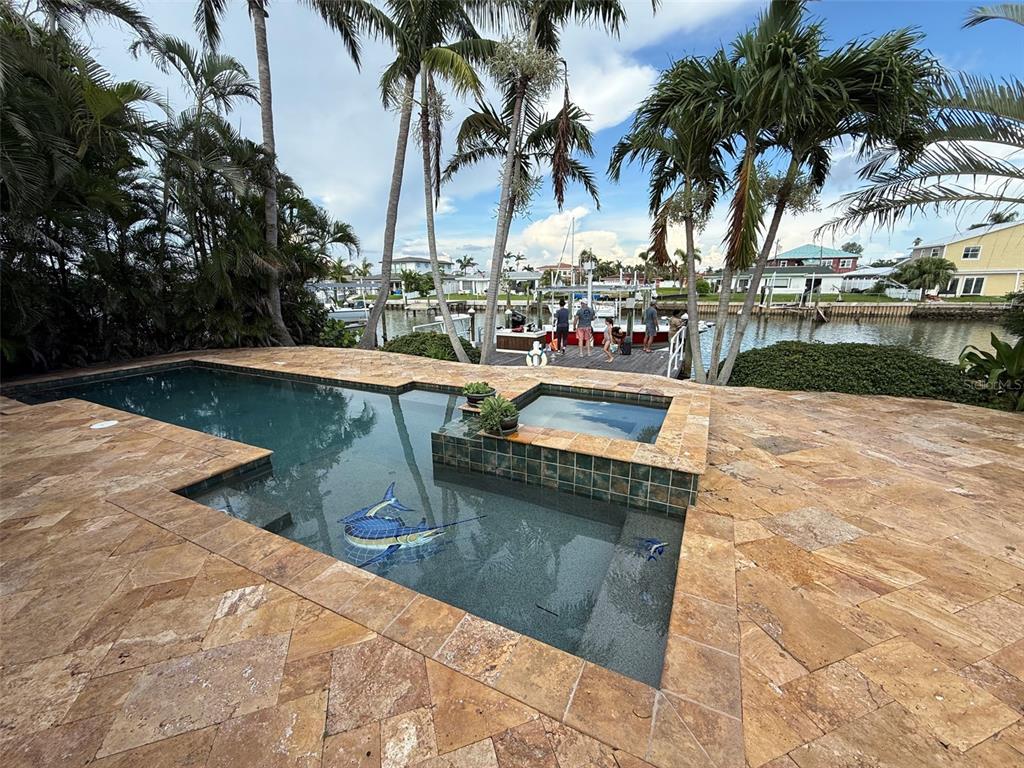 A swimming pool and spa with stone decking overlook a canal with a private dock — 639 NORMANDY ROAD, MADEIRA BEACH, FL