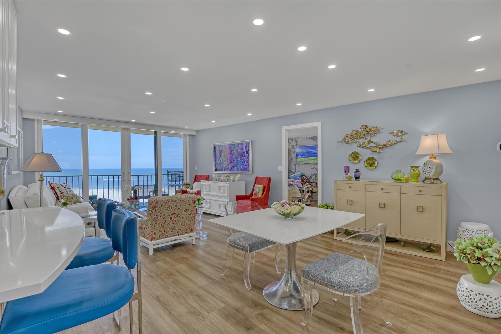 A bright dining and living area features a white table, blue chairs, and ocean views — 100 Ocean Trail Way # 1002, Jupiter FL 33477, JUPITER, FL