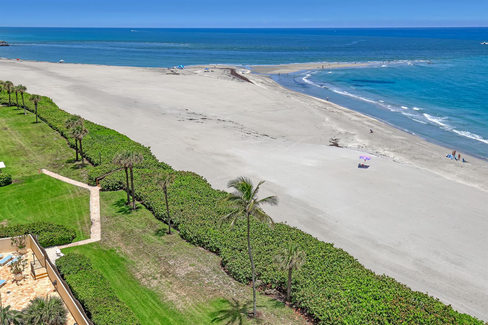 An aerial view shows a sandy beach, ocean, and a landscaped lawn with palm trees — 100 Ocean Trail Way # 1002, Jupiter FL 33477, JUPITER, FL
