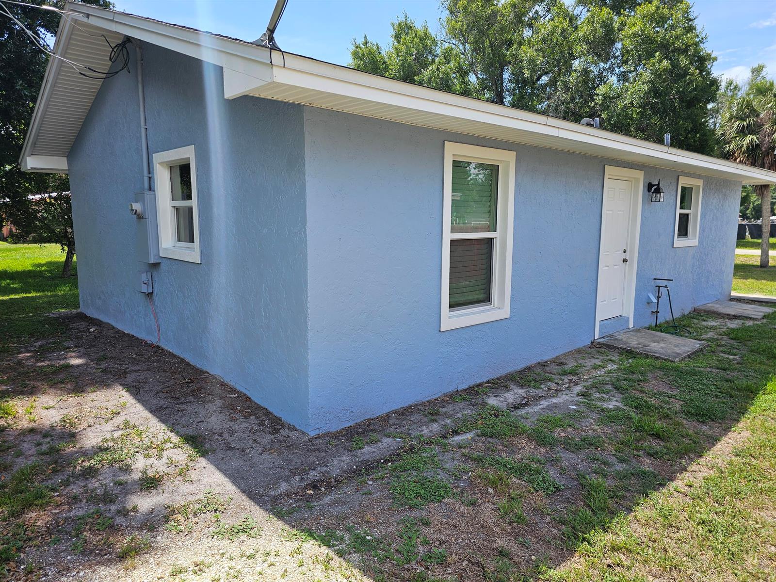 The exterior of a blue, single-story house features white trim, windows, and a side door — 1749 NE 2nd Street, Okeechobee FL 34972, OKEECHOBEE, FL