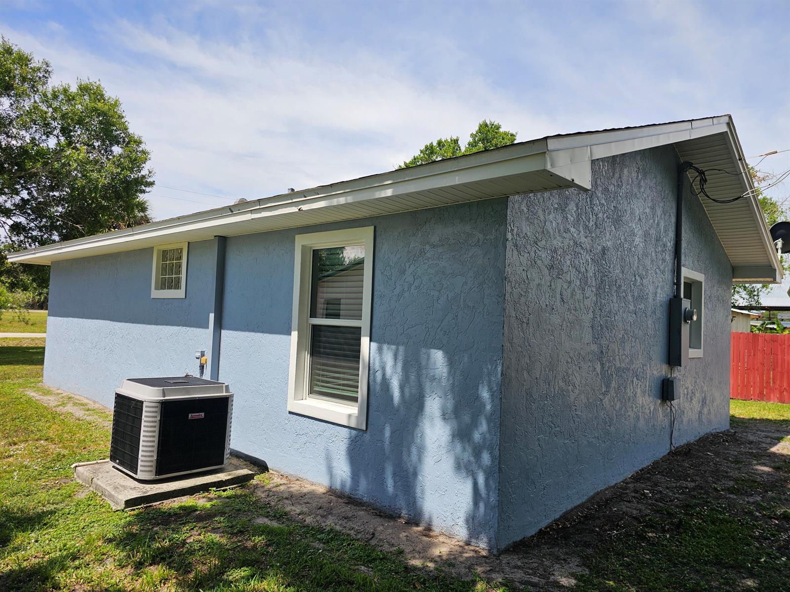 The exterior of a blue stucco house features a window, an AC unit, and a roof — 1749 NE 2nd Street, Okeechobee FL 34972, OKEECHOBEE, FL