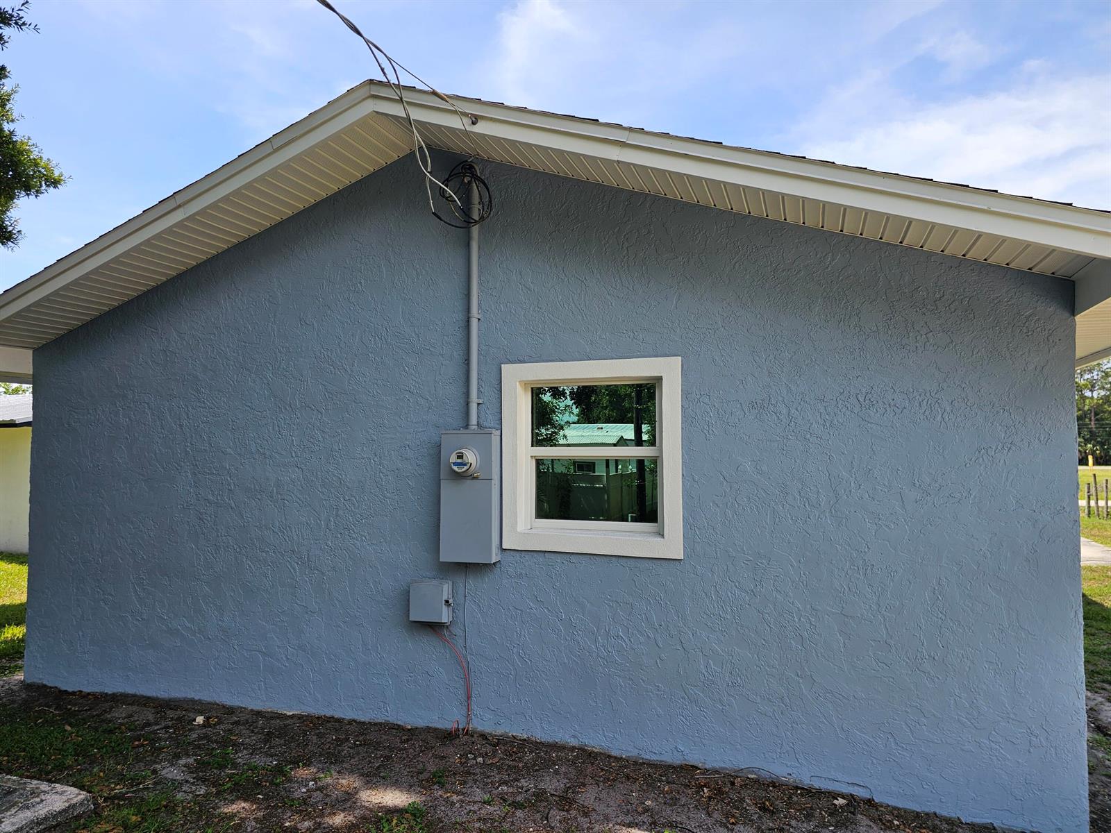 The exterior of a blue stucco house features a window, an electrical meter, and soffits — 1749 NE 2nd Street, Okeechobee FL 34972, OKEECHOBEE, FL