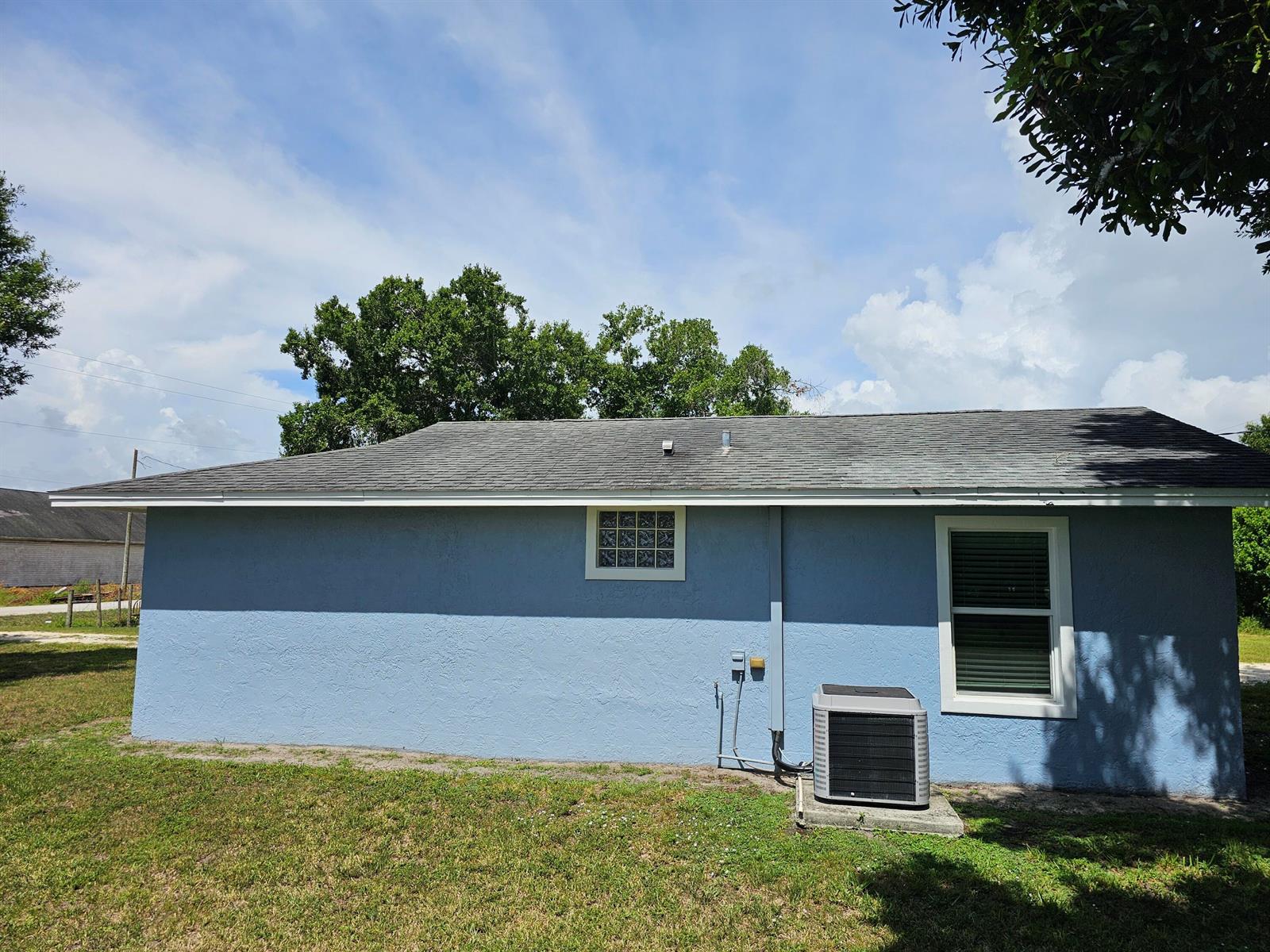 The exterior of a blue stucco house features a glass block window and an AC unit — 1749 NE 2nd Street, Okeechobee FL 34972, OKEECHOBEE, FL