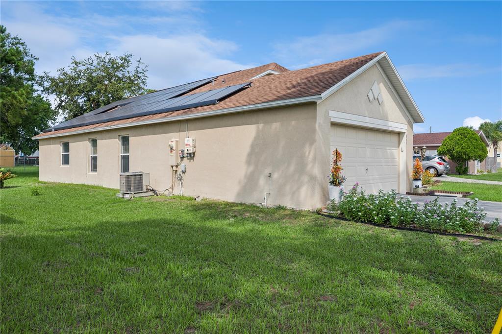 The exterior of a tan house features a garage, solar panels, and a grassy yard — 663 MESILLA DRIVE, KISSIMMEE, FL