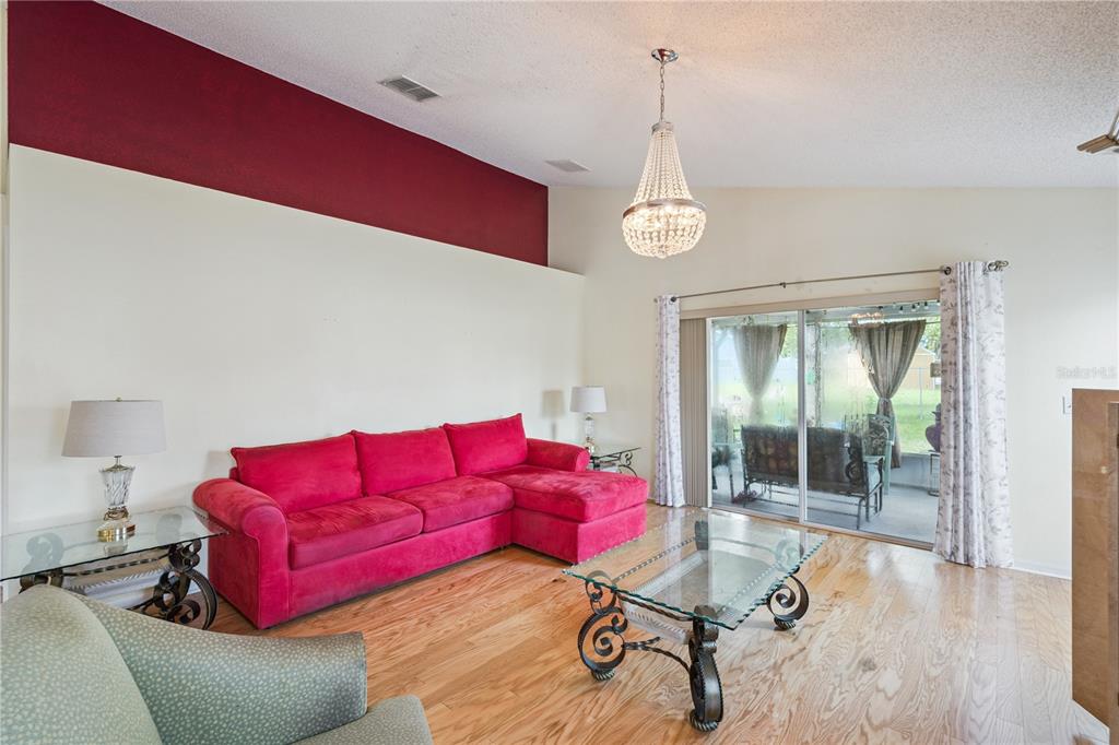 A living room features a red sectional sofa, glass coffee table, and a crystal chandelier — 663 MESILLA DRIVE, KISSIMMEE, FL