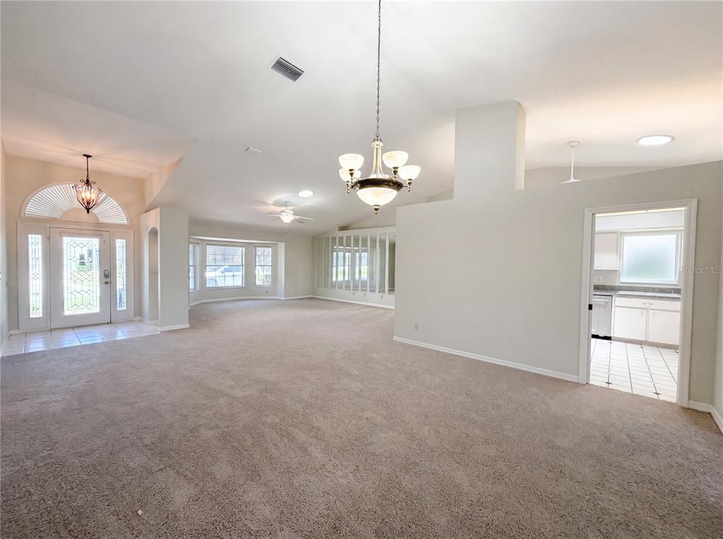 A spacious living room features beige carpeting, a chandelier, and an entryway with a door — 27305 RACQUET CIRCLE, LEESBURG, FL