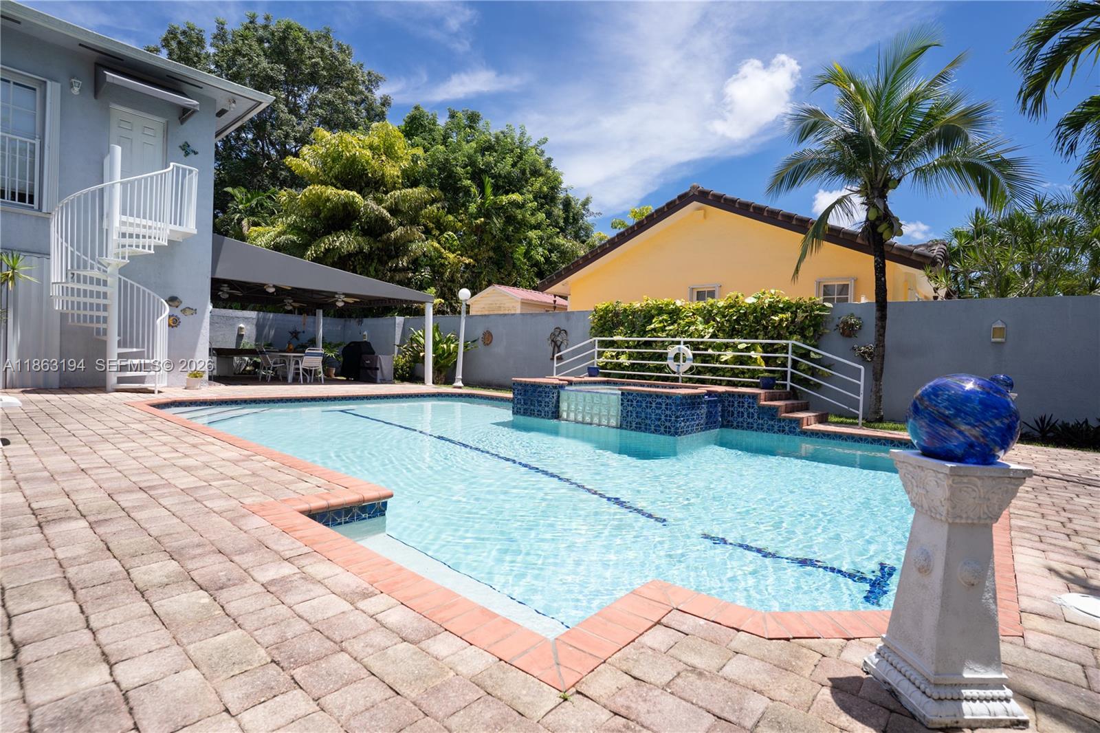 A backyard swimming pool features a raised spa, brick pavers, and a white spiral staircase — 11680 SW 92nd St, Miami FL 33176, MIAMI, FL