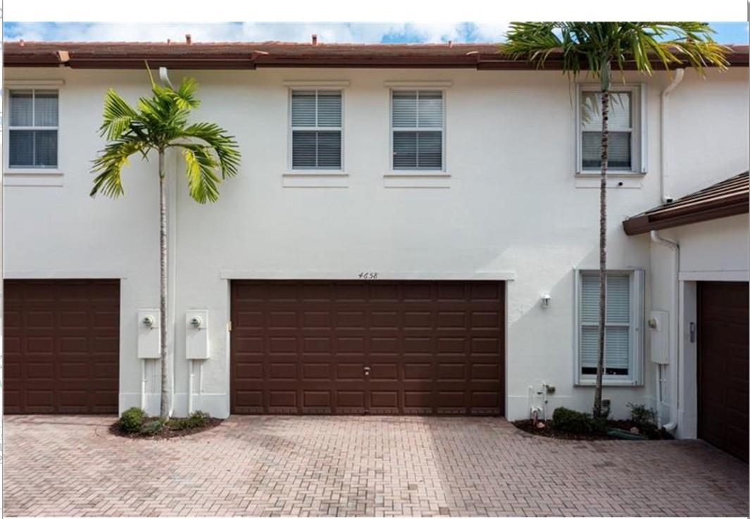A two-story townhouse exterior features a brown garage door, white stucco walls, and palm trees — 4658 Monarch Way, Coconut Creek FL 33073, COCONUT CREEK, FL