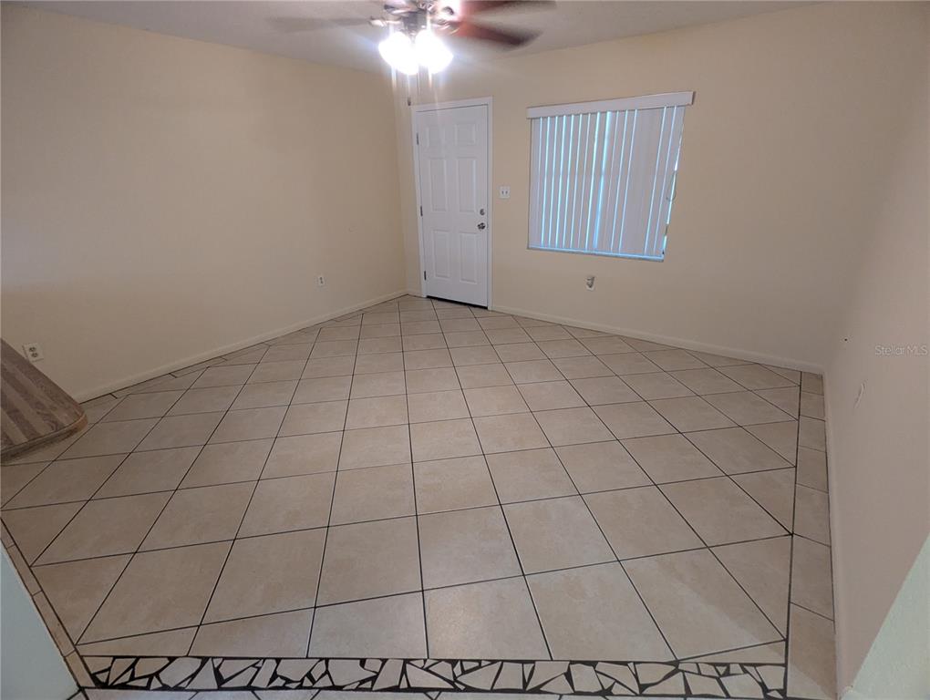 An empty room with beige tile flooring, a ceiling fan, and a white entry door — 824 N SAINT CLAIR ABRAMS AVENUE, TAVARES, FL