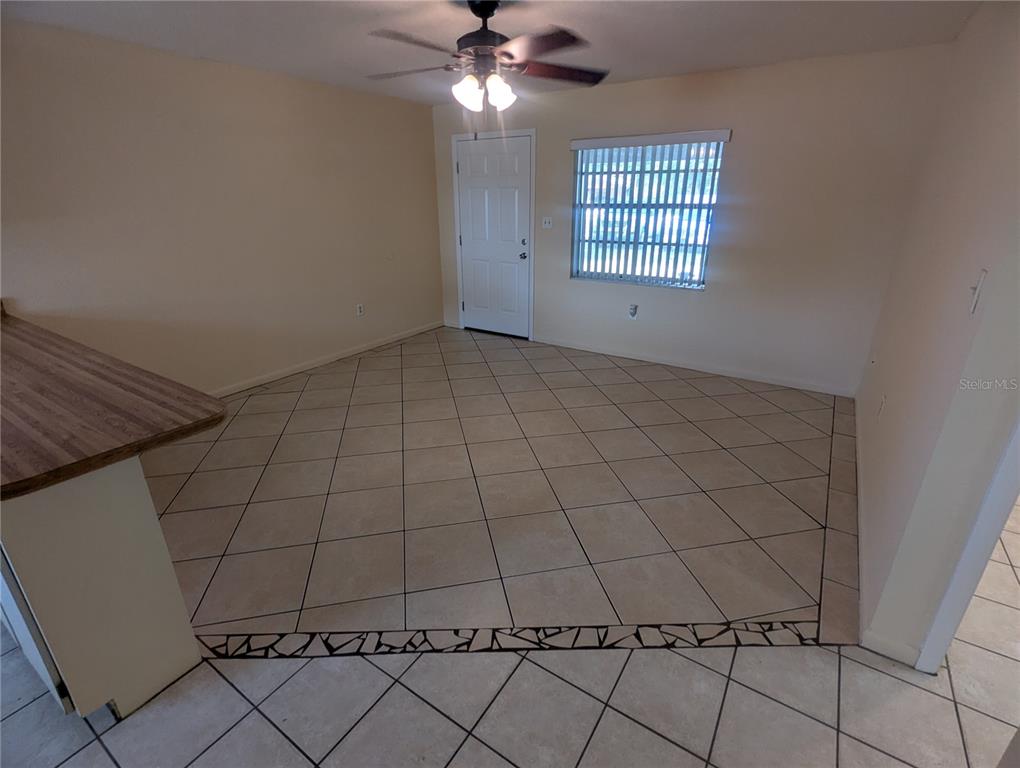 An empty room features beige tile flooring, a ceiling fan, and a white entry door — 824 N SAINT CLAIR ABRAMS AVENUE, TAVARES, FL