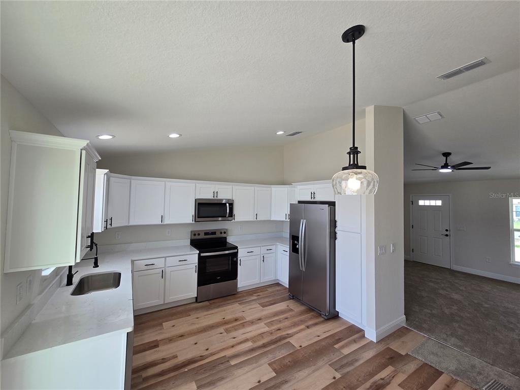 A kitchen with white cabinets, stainless steel appliances, and wood-look flooring — 3 WALNUT RUN COURT, OCALA, FL