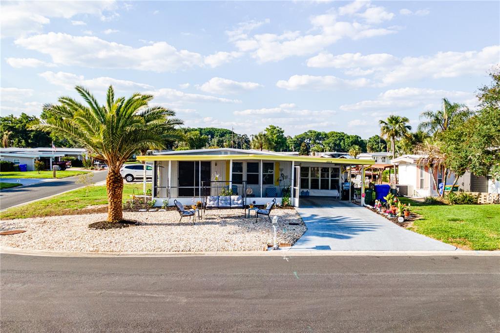 A single-story manufactured home with a palm tree, gravel front yard, and attached carport — 1004 TODD WAY, TAVARES, FL