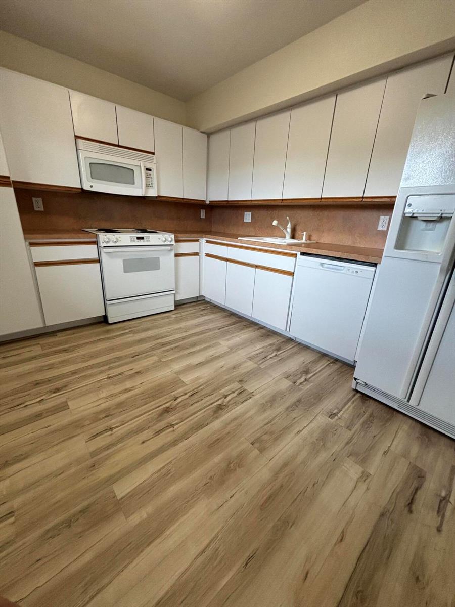 A kitchen features white cabinets, white appliances, a brown backsplash, and wood-look flooring — 555 Oaks Lane # 309, Pompano Beach FL 33069, POMPANO BEACH, FL