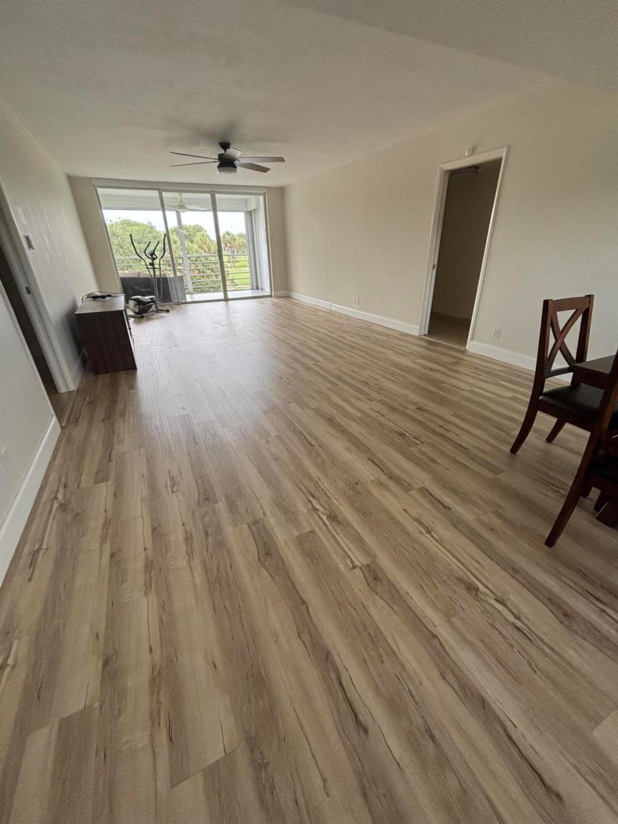 An open living area features light wood-look flooring, a ceiling fan, and a sliding glass door — 555 Oaks Lane # 309, Pompano Beach FL 33069, POMPANO BEACH, FL