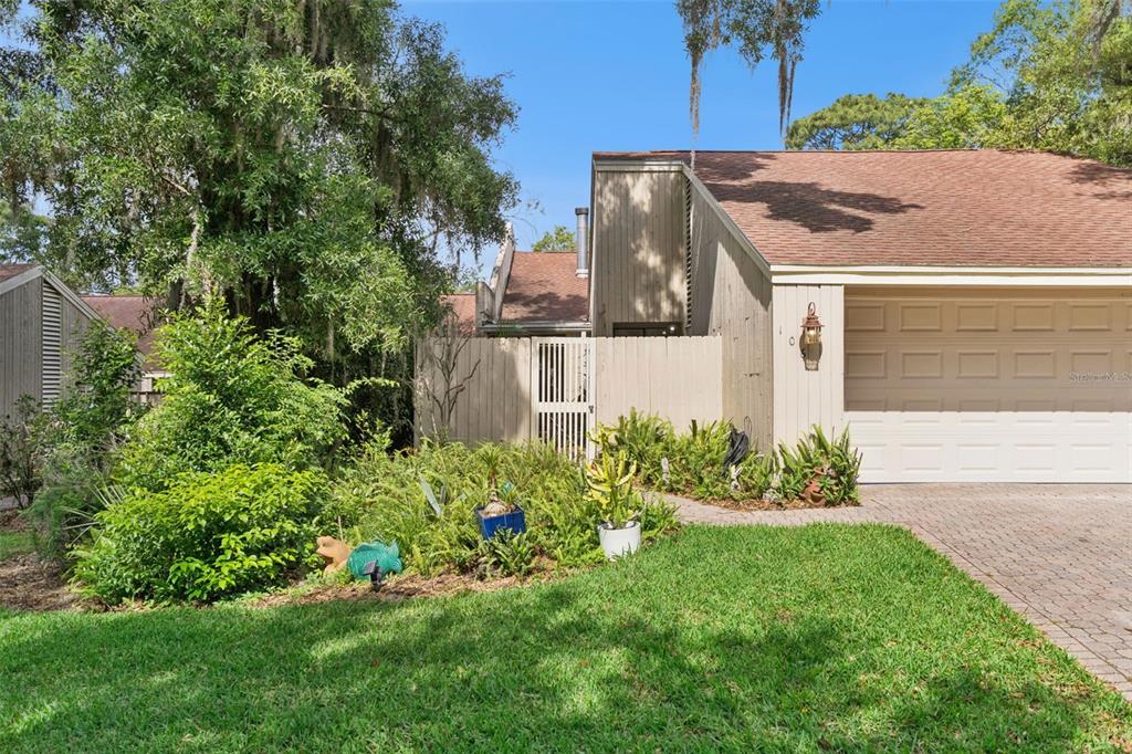 A tan house with a garage and a fenced courtyard surrounded by trees and landscaping — 106 HIDDEN OAK DRIVE, LONGWOOD, FL