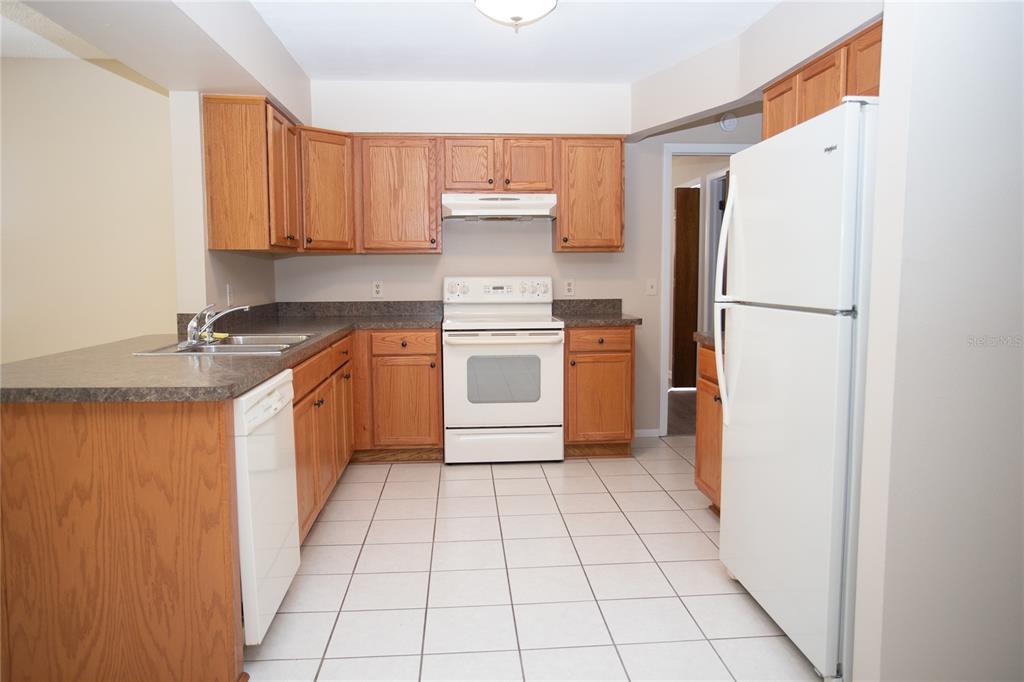 A kitchen with oak cabinets, white appliances, a tiled floor, and a laminate countertop — 10124 CARRIN ROAD, SPRING HILL, FL