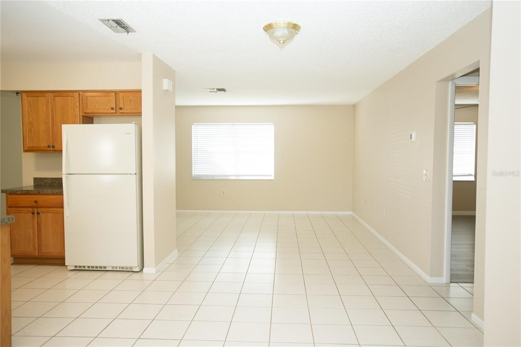 A kitchen with wood cabinets and a white refrigerator opens into a tiled dining area — 10124 CARRIN ROAD, SPRING HILL, FL