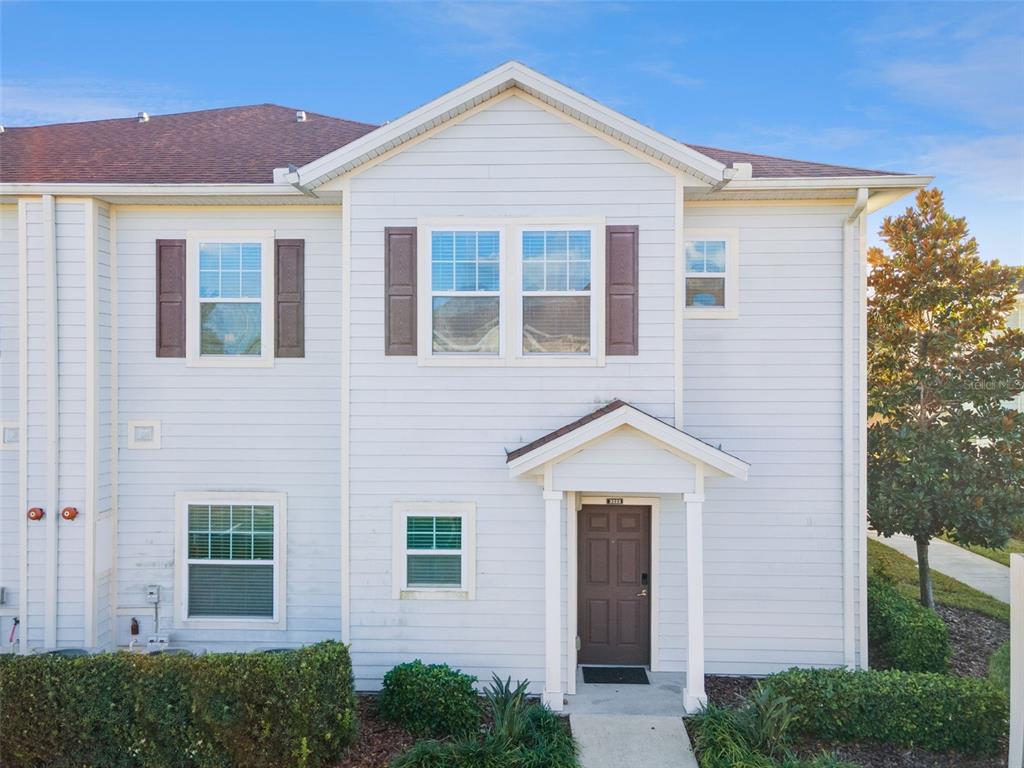 A two-story townhouse exterior with light siding, brown shutters, and a covered front entryway — 3222 CUPID PLACE, KISSIMMEE, FL