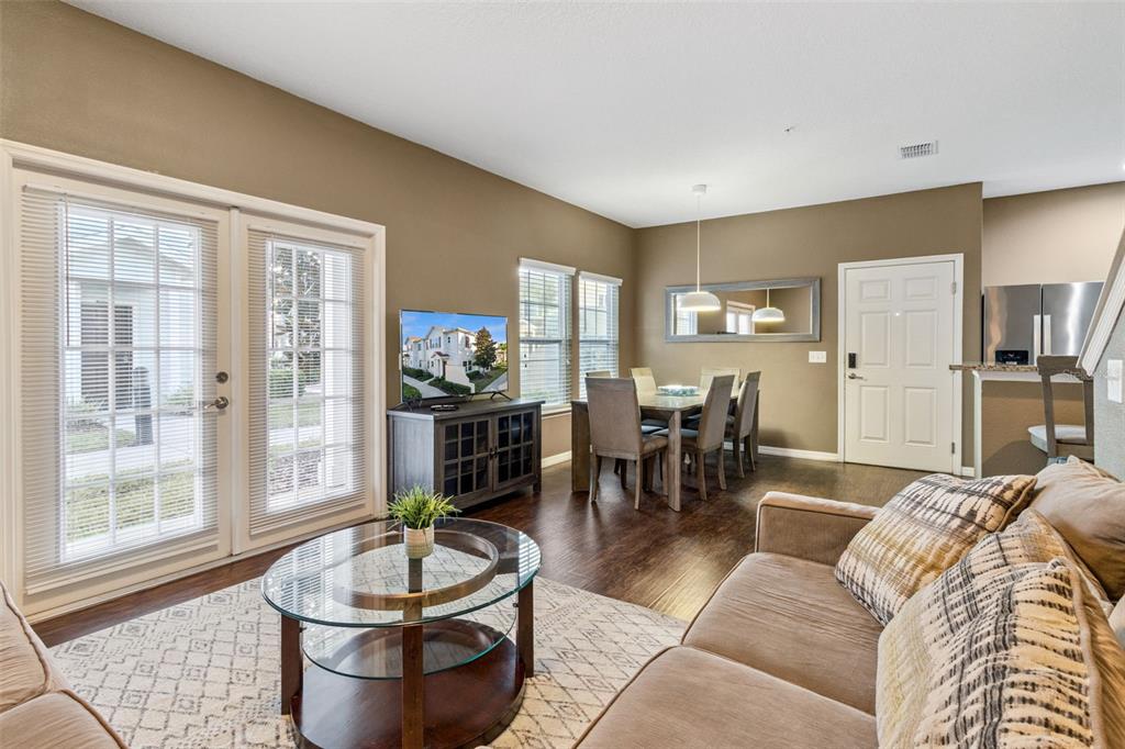 A living room and dining area with brown walls, dark wood floors, and glass doors — 3222 CUPID PLACE, KISSIMMEE, FL