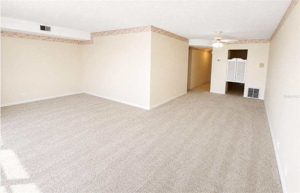 A spacious, carpeted living room features beige walls, a ceiling fan, and a hallway entrance — 1847 SHORE DRIVE S UNIT 710, SOUTH PASADENA, FL