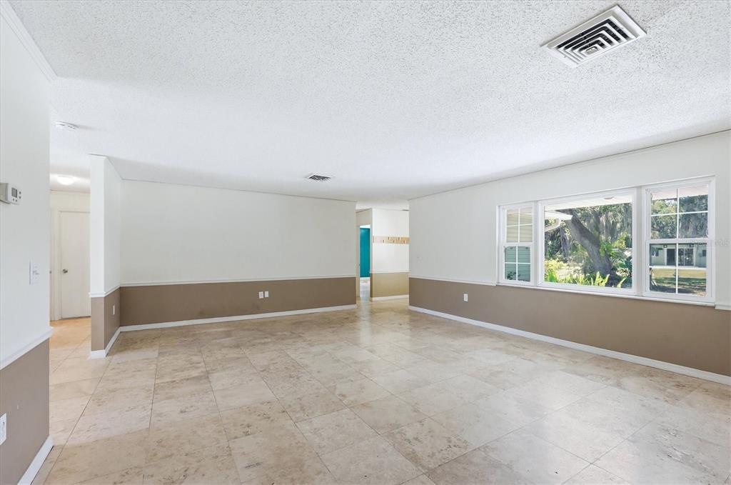 An empty room with beige tile floors, white walls, and a brown wainscot border — 4420 GREENWOOD STABLES ROAD, SARASOTA, FL