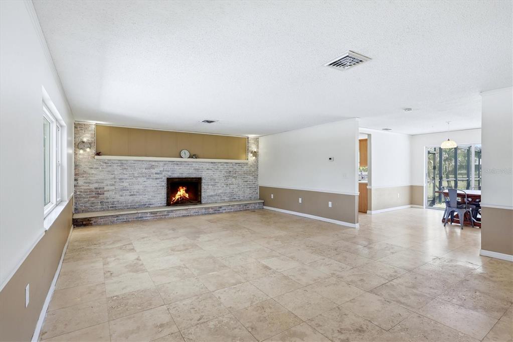 A spacious living room features a brick fireplace, tile flooring, and a dining area beyond — 4420 GREENWOOD STABLES ROAD, SARASOTA, FL