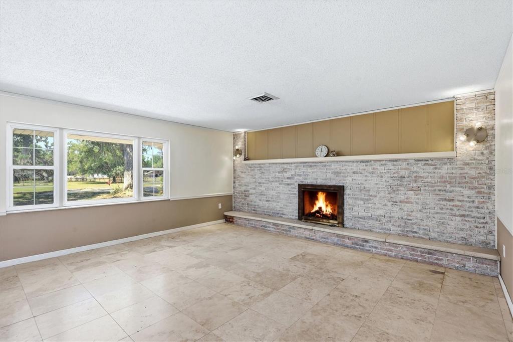A living room features a white brick fireplace, tile flooring, and a large picture window — 4420 GREENWOOD STABLES ROAD, SARASOTA, FL
