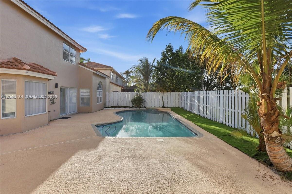 A backyard features a swimming pool, a tan patio, and a white fence — 13209 NW 12th Ct, Sunrise FL 33323, SUNRISE, FL