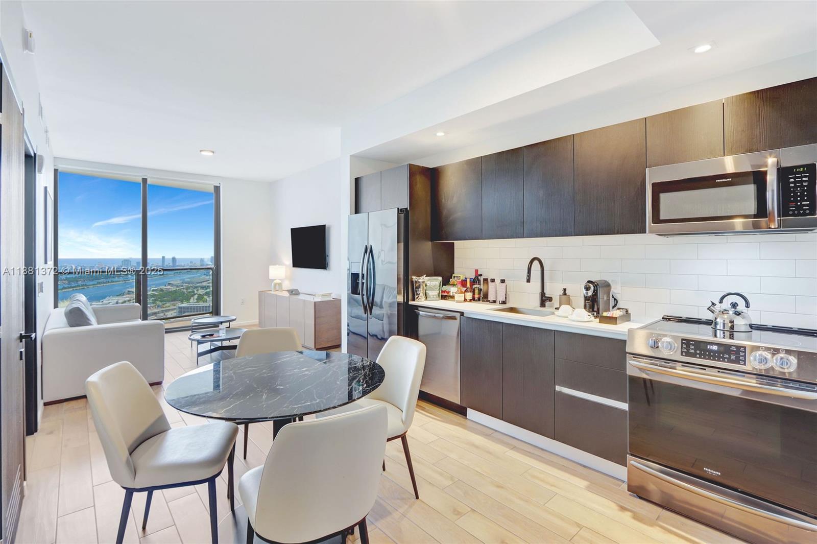 A modern kitchen and dining area with dark cabinetry, stainless appliances, and a city view — 398 NE 5th St # 3810, Miami FL 33132, MIAMI, FL