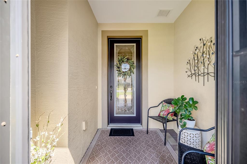 A covered entryway features a dark front door with glass inlay, a rug, and seating — 6707 SW 95TH CIRCLE, OCALA, FL