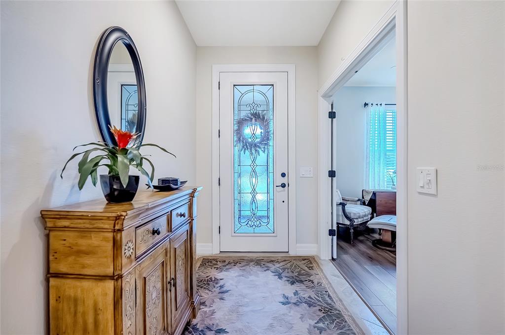 An entryway features a wooden sideboard, an oval mirror, a patterned rug, and a glass-paneled door — 6707 SW 95TH CIRCLE, OCALA, FL
