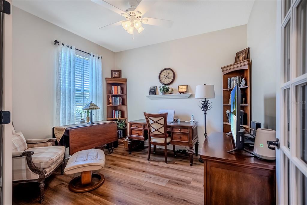A home office features wood-look flooring, a wooden desk, two bookcases, and a comfortable armchair — 6707 SW 95TH CIRCLE, OCALA, FL