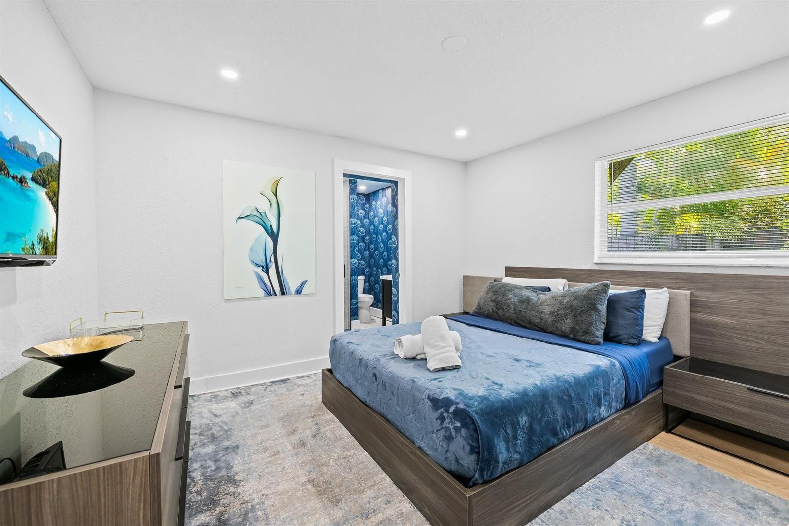 A bedroom features a blue bed, a wall-mounted television, and an attached bathroom with wallpaper — 415 SE 3rd Avenue, Delray Beach FL 33483, DELRAY BEACH, FL