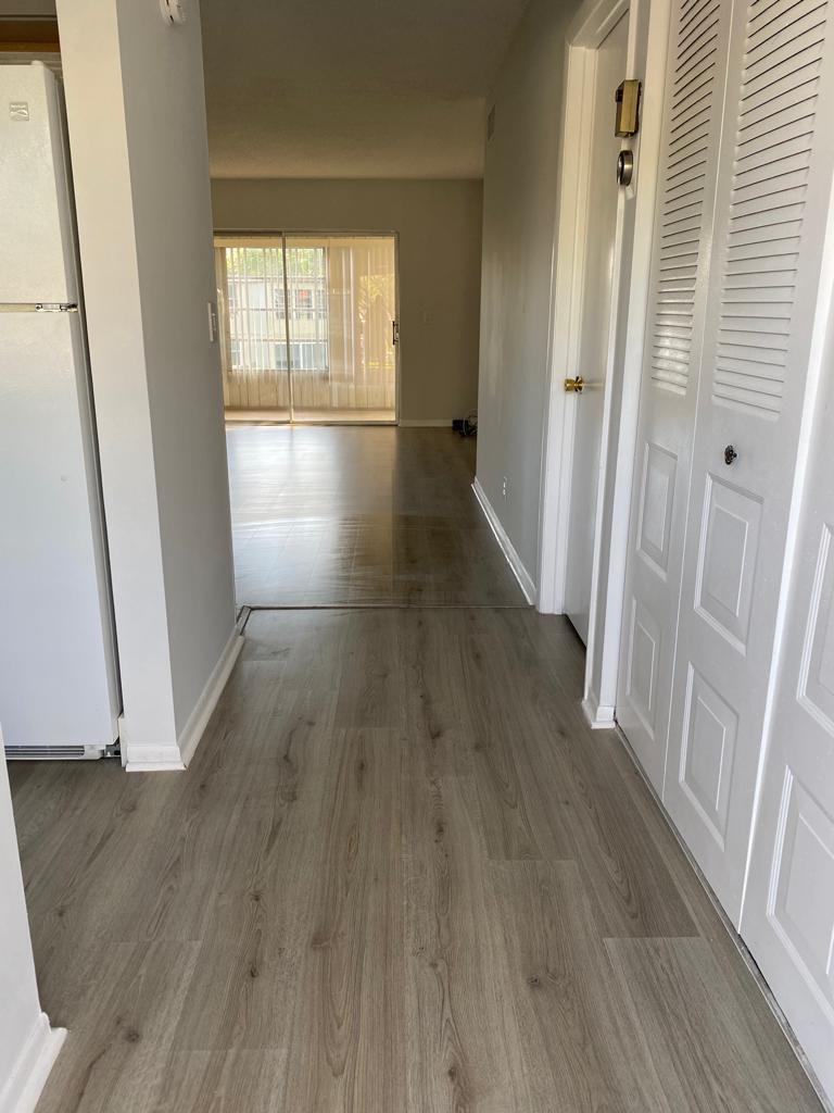 A hallway with light wood-look flooring leads toward a living area with a sliding glass door — 19 Abbey Lane # 206, Delray Beach FL 33446, DELRAY BEACH, FL