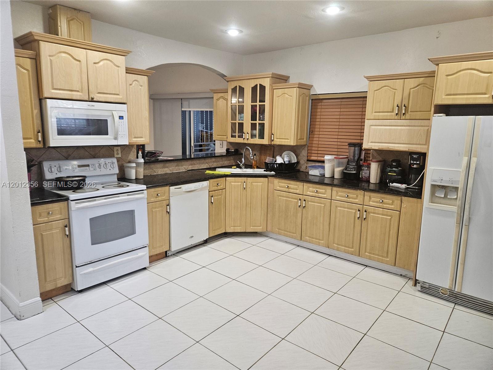 A kitchen features light wood cabinets, white appliances, dark countertops, and white tiled flooring — 2231 NW 4th Ter, Miami FL 33125, MIAMI, FL
