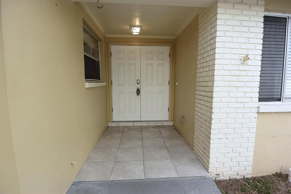 A covered entryway features double white doors, tiled flooring, and a white brick exterior wall — 8235 DONALDSON DRIVE, TAMPA, FL