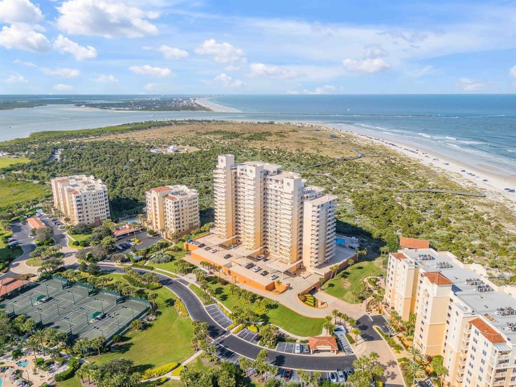 An aerial view shows several high-rise residential buildings surrounded by coastal vegetation and tennis courts — 257 MINORCA BEACH WAY UNIT 506, NEW SMYRNA BEACH, FL