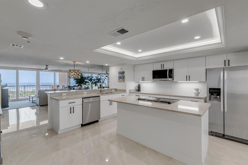 A modern white kitchen with stainless steel appliances and an island overlooks a beach view — 257 MINORCA BEACH WAY UNIT 506, NEW SMYRNA BEACH, FL