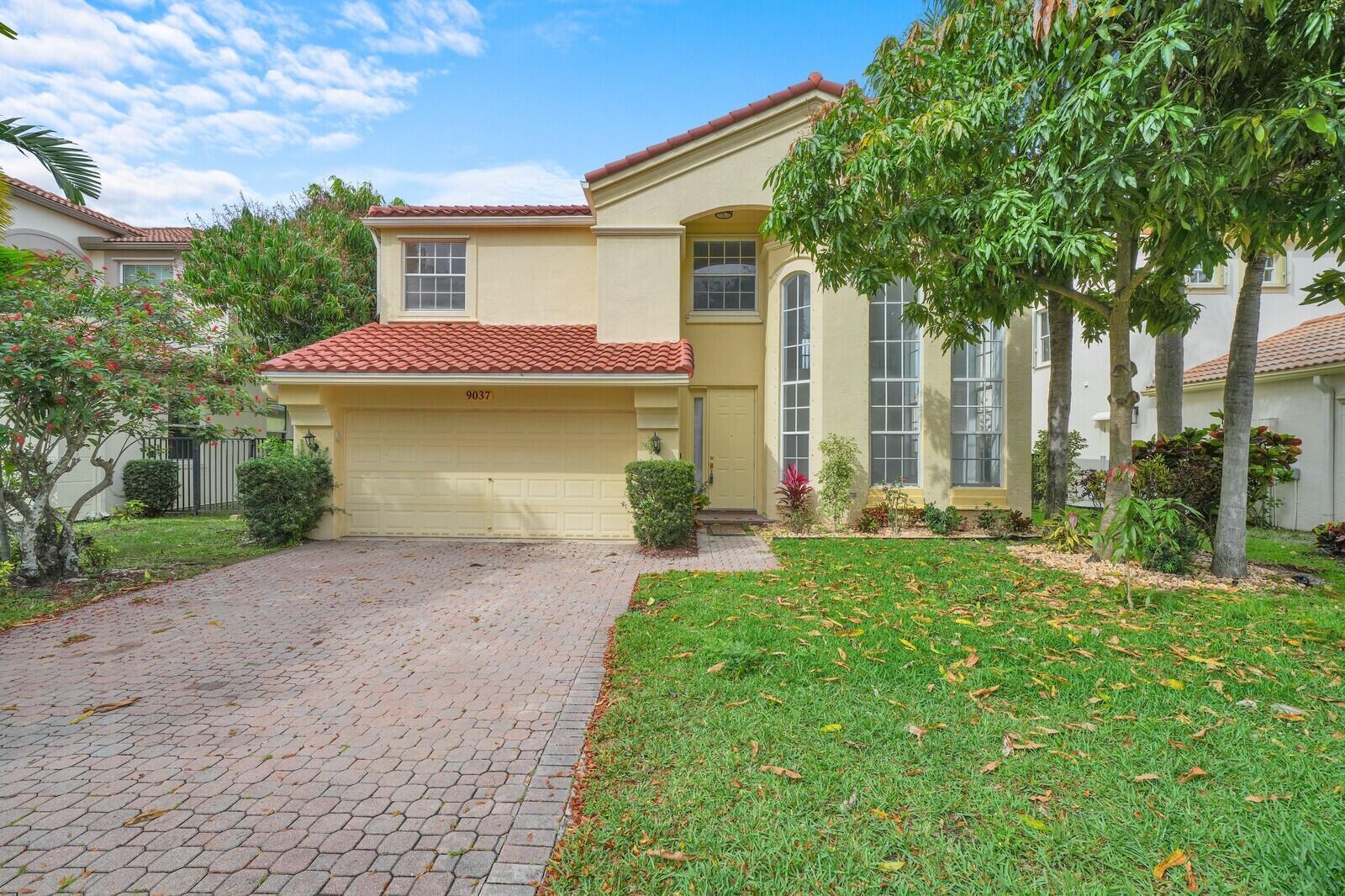 A two-story yellow house with a tiled roof, a garage, and a brick driveway — 9037 Alexandra Circle, Wellington FL 33414, WELLINGTON, FL