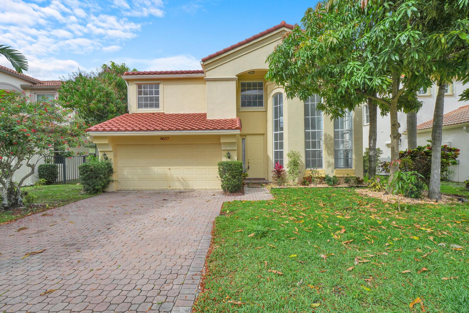 A two-story house with a red tile roof, yellow stucco exterior, and a brick driveway — 9037 Alexandra Circle, Wellington FL 33414, WELLINGTON, FL