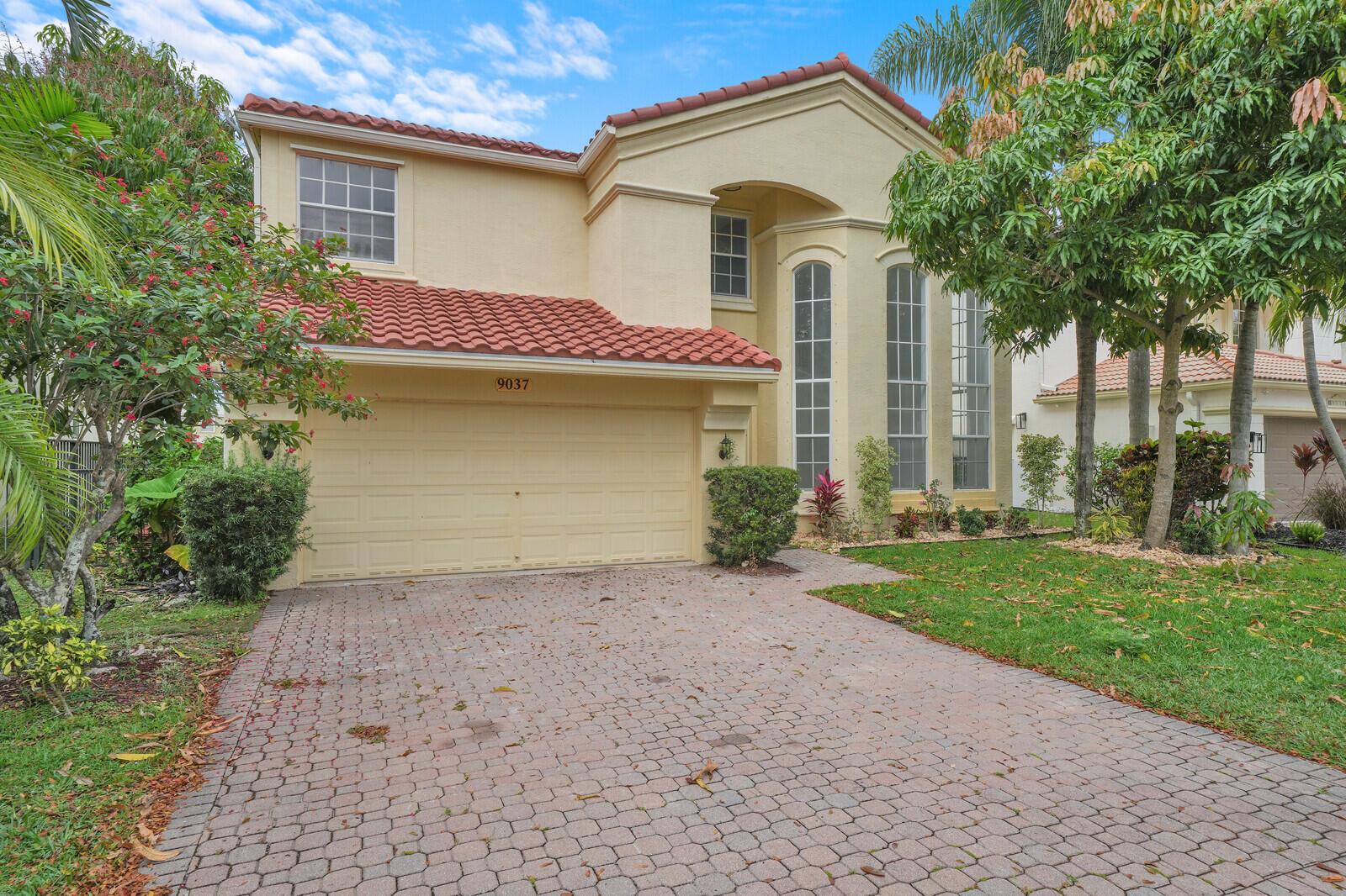 A two-story house with a tan stucco exterior, red tile roof, and a paved driveway — 9037 Alexandra Circle, Wellington FL 33414, WELLINGTON, FL