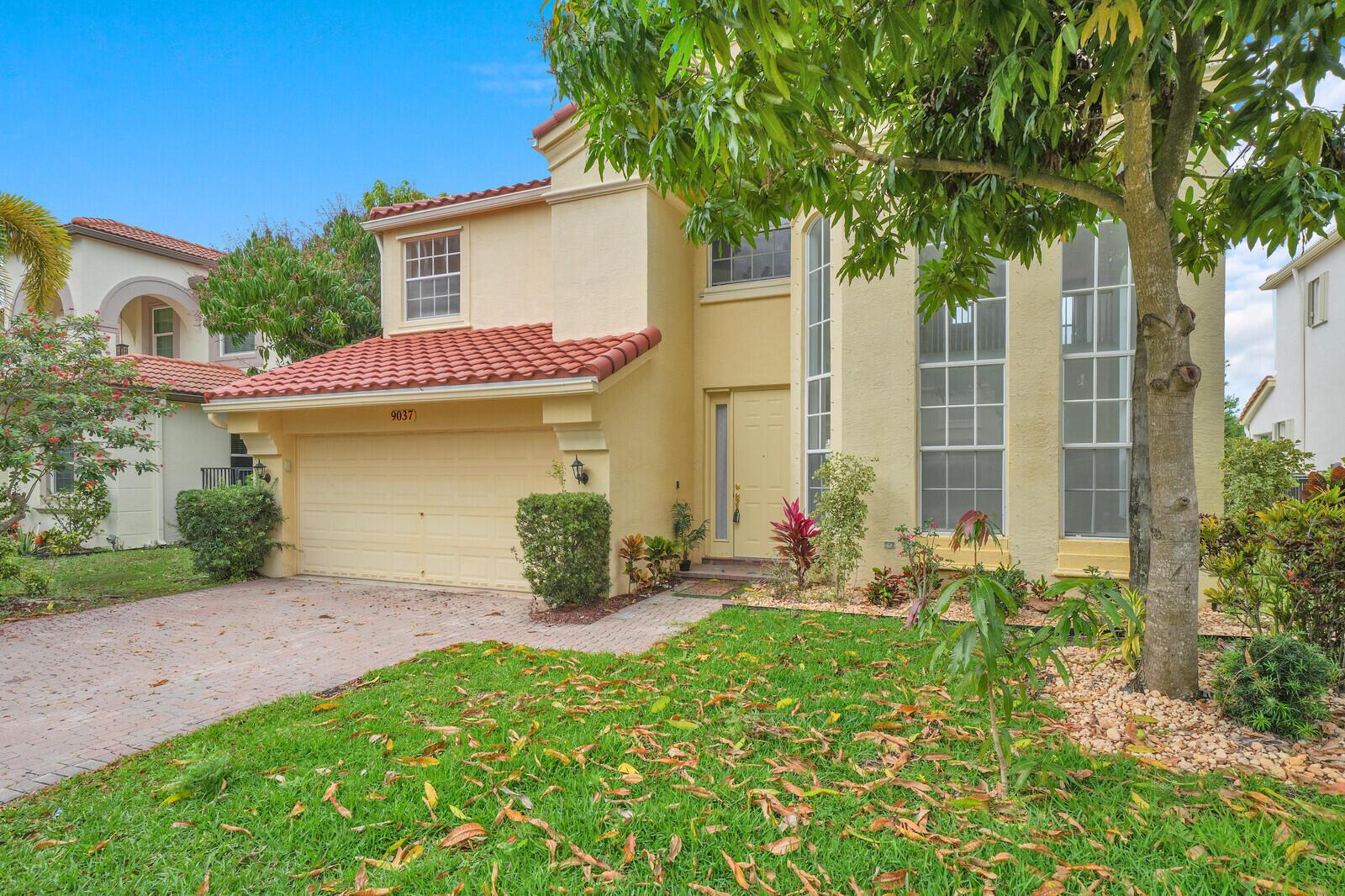 A two-story yellow stucco house with a red tile roof and a paved driveway — 9037 Alexandra Circle, Wellington FL 33414, WELLINGTON, FL