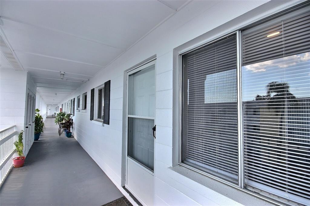 An exterior walkway with white walls, a screen door, and windows with closed blinds — 1631 LEISURE DRIVE UNIT M36, BRADENTON, FL