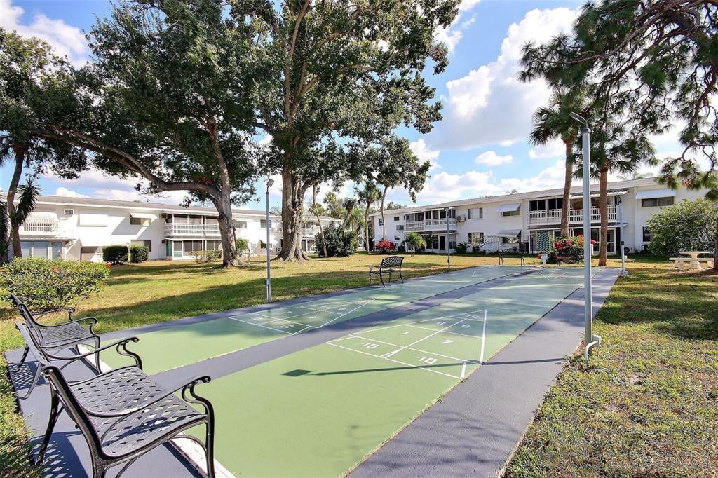 An outdoor shuffleboard court sits on a grassy lawn between two-story apartment buildings — 1631 LEISURE DRIVE UNIT M36, BRADENTON, FL