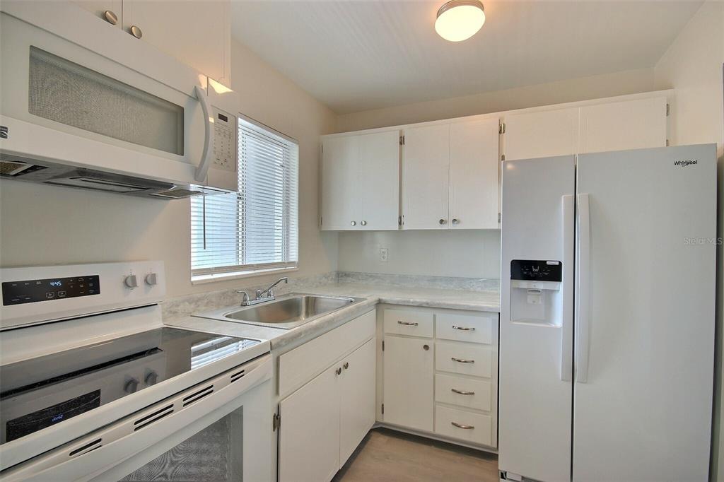 A kitchen with white cabinets, white appliances, a stainless steel sink, and light countertops — 1631 LEISURE DRIVE UNIT M36, BRADENTON, FL
